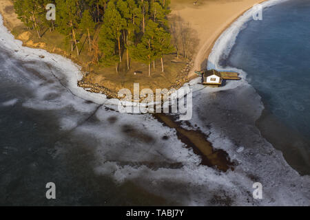 Vue aérienne de la rive du lac gelé et petit chalet en hiver sur la journée ensoleillée. Banque D'Images