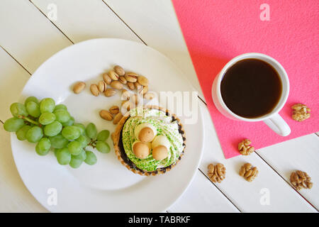 Une grappe de raisins, pistaches, noix tasse avec du café noir sur un fond de bois blanc à côté d'une serviette rose. Pays hôtes. La lumière du jour. Banque D'Images