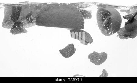 Image Gros plan noir et blanc d'oranges et des feuilles de menthe flottant dans l'eau. La chute des fruits et les projections d'eau. Banque D'Images