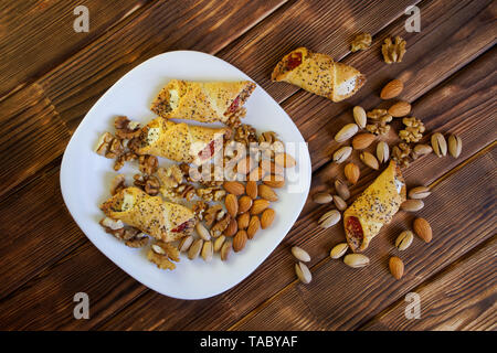 Des biscuits sucrés avec de la confiture, un mélange de pistaches, amandes et noix se trouvent dans une assiette blanche sur une table en bois faites de planches de pin. La récolte de la ferme. Da Banque D'Images