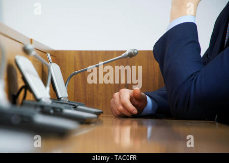 Un politicien ou homme d'affaires en costume est assis à une table en bois poli devant un microphone au cours d'une discussion, devoir, ou de présentation. Sans f Banque D'Images