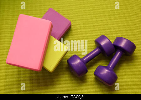 Outils de remise en forme - vert, rose et violet cubes et les haltères sur un tapis vert Banque D'Images