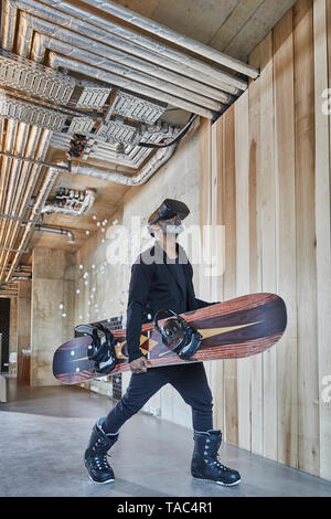 Mature businessman portant des lunettes VR holding snowboard in modern office Banque D'Images