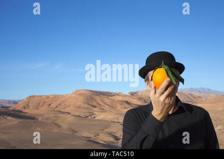 Le Maroc, la vallée de l'Ounila, un homme portant un chapeau melon tenant une orange en face de son visage Banque D'Images