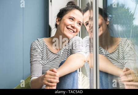 Smiling woman looking out of window at home Banque D'Images