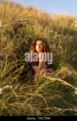 Pensive young woman crouching in meadow Banque D'Images