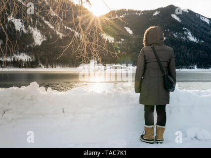 L'Autriche, le Tyrol, l'Achensee, femme debout au bord du lac au coucher du soleil en hiver Banque D'Images