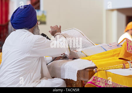 Un prêtre dans le turban sikh lit depuis le livre saint, le Guru Granth Sahib, et tourne une page. À RICHMOND HILL, Queens, New York. Banque D'Images