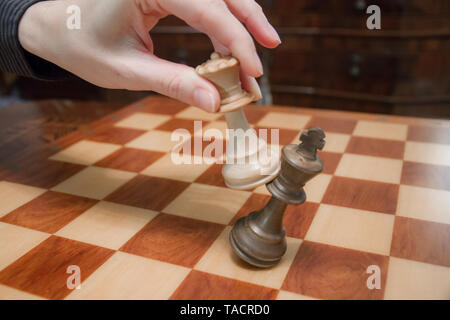 Concept : la femme qui domine l'homme. A woman's hand checkmate donne au roi avec la reine sur un échiquier en bois, avec aucune autre pièce en pl Banque D'Images