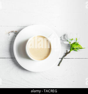 Une tasse de café aromatique et d'épanouissement branches d'un pommier sur un fond blanc en bois. Mise à plat. Banque D'Images