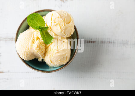 Boules de crème glacée à la vanille avec les feuilles de menthe dans un bol turquoise sur une table en bois blanc Banque D'Images