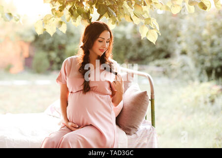 Smiling pregnant woman holding élégante robe rose ventre à l'extérieur. La maternité. La maternité. Banque D'Images