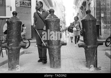 Un homme aveugle avec bâton blanc fait son chemin passé canon coincé dans le sol dans la Vieille Havane, Cuba Banque D'Images