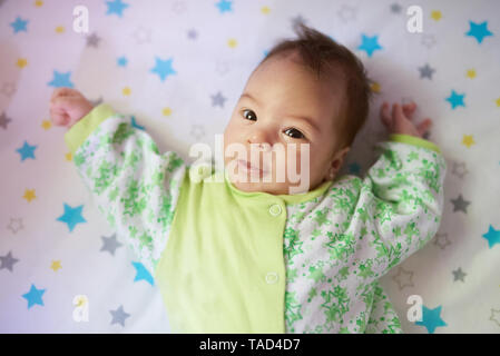 Close-up portrait of baby girl laying on bed in sunny day Banque D'Images