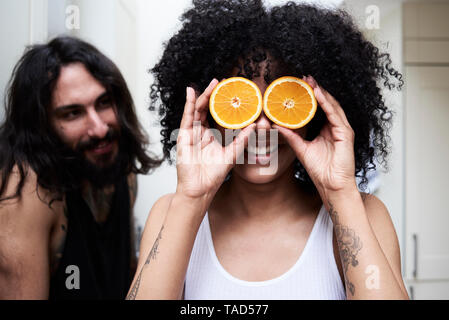 Happy young woman couvrant ses yeux avec des oranges dans la cuisine Banque D'Images