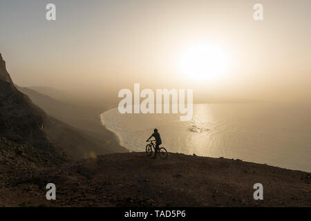 L'Espagne, Lanzarote, mountainbiker sur un voyage à la côte au coucher du soleil en profitant de la vue Banque D'Images