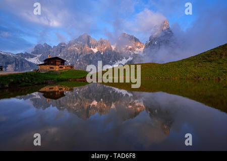 L'Italie, Trentino, Dolomites, Passo Rolle, Pale di San Martino, Cimon della Pala avec Baita Segantini reflétant dans petit lac dans la soirée Banque D'Images