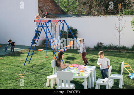 Les enfants jouant dans un jardin, peinture des oeufs de Pâques, l'escalade sur le swing Banque D'Images