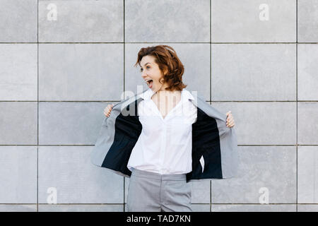 Portrait of a young businesswoman crier en face de mur avec des carreaux gris, ouvrant sa veste Banque D'Images