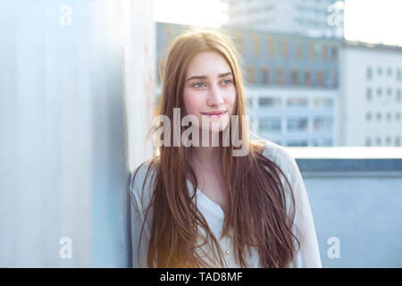 Portrait of smiling young woman leaning against a wall