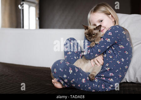 Portrait of smiling little girl wearing pyjamas avec floral design holding cat Banque D'Images