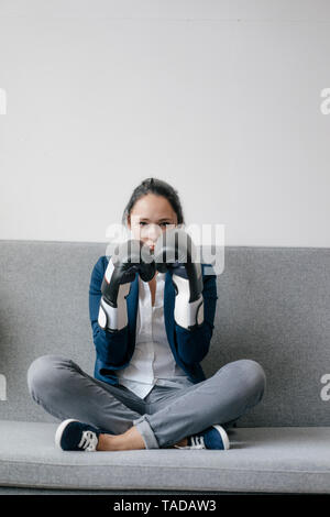 Portrait of young woman sitting on couch wearing boxing gloves Banque D'Images