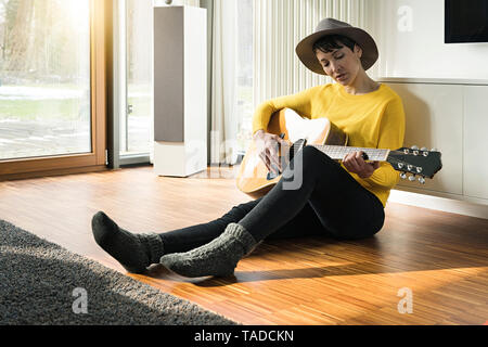 Femme assise sur le plancher de salle de séjour qui joue de la guitare Banque D'Images