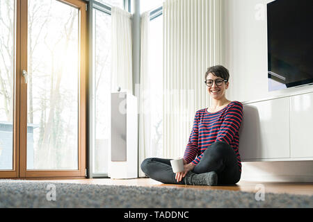 Portrait of laughing woman assis sur le plancher de salle de séjour Banque D'Images