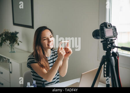 Videoblogger Fille beauté ou blogger enregistre une vidéo pour les abonnés. Rouge à lèvres, elle montre et raconte comment l'utiliser correctement. Banque D'Images