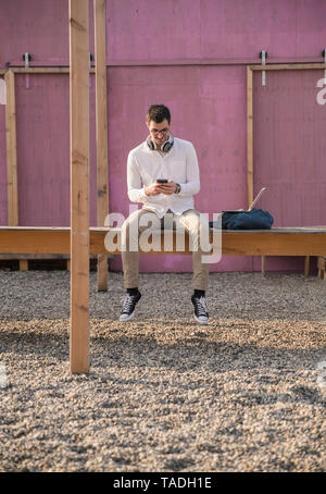 Jeune homme assis sur la plate-forme using cell phone Banque D'Images