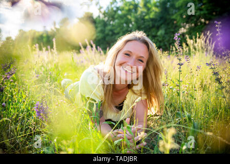 Portrait of happy blonde woman lying on flower meadow en été Banque D'Images