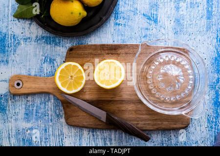 Deux moitiés de citron, couteau de cuisine et presse-citron sur planche de bois Banque D'Images