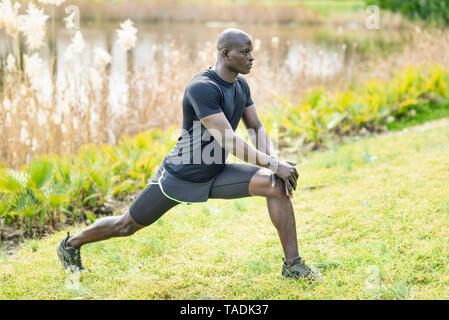 L'homme en noir sportswear doing stretching exercice sur un pré Banque D'Images