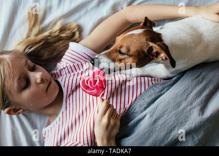 Girl lying on bed watching her dog licking lollipop Banque D'Images