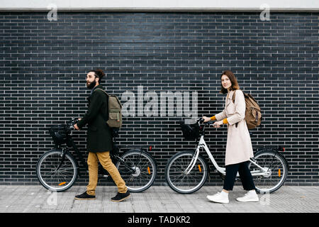 Couple poussant les vélos électriques le long d'un mur de brique Banque D'Images