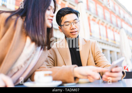 Espagne, Madrid, jeune couple à l'aide de téléphone cellulaire dans un café sur la Plaza Mayor Banque D'Images