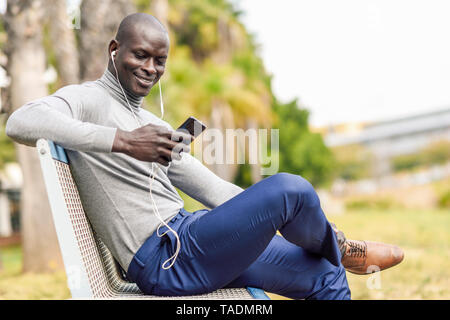 Portrait of smiling businessman assis sur un banc, écouter la musique avec vos écouteurs et smartphone Banque D'Images