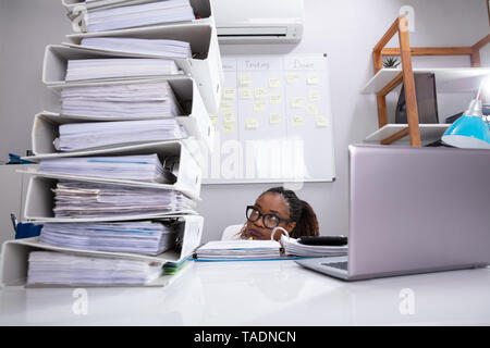 Close-up of Businesswoman se cacher derrière le bureau avec une pile de dossiers et ordinateur portable Banque D'Images