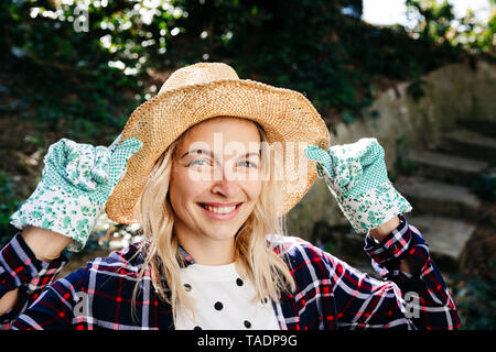 Jeune femme blonde avec chapeau de paille et des gants de jardinage vert Banque D'Images