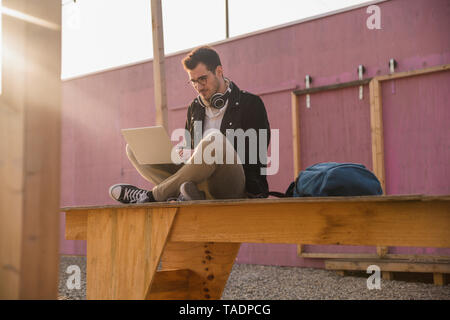 Jeune homme assis sur la plate-forme à l'aide d'ordinateur portable Banque D'Images