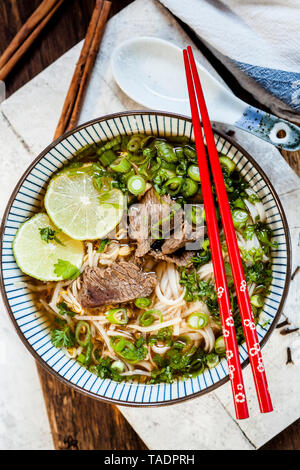 Bol de Pho vietnamien avec des nouilles de riz, haricots mungo, coriandre, oignons de printemps et limes Banque D'Images