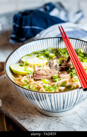 Bol de Pho vietnamien avec des nouilles de riz, haricots mungo, coriandre, oignons de printemps et limes Banque D'Images