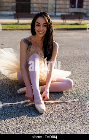 L'Italie, Vérone, portrait of smiling ballerine assis dans la ville mise sur les chaussures de ballet Banque D'Images