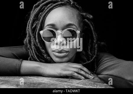 Portrait de femme avec des dreadlocks portant des lunettes de soleil en face de fond noir Banque D'Images