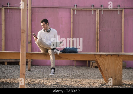 Jeune homme assis sur la plate-forme using cell phone Banque D'Images