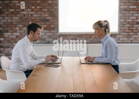 Businessman and woman sitting at desk, working on laptop Banque D'Images