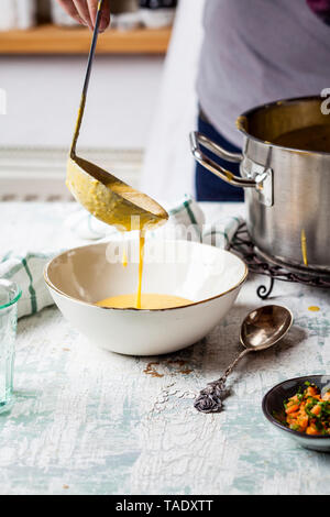 Woman pouring creme de carottes dans un bol, vue partielle Banque D'Images