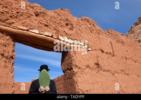 Le Maroc, Aït-Ben-Haddou, un homme portant un chapeau melon tenant une feuille de cactus en face de son visage Banque D'Images