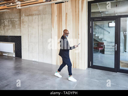 Mature businessman with cell phone walking in modern office Banque D'Images