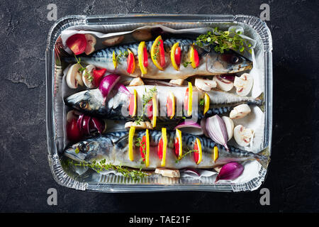 Trois matières le maquereau au citron, tomates, champignons, épices et herbes. scomber préparé pour la cuisson dans un moule en aluminium sur une table en béton, Banque D'Images